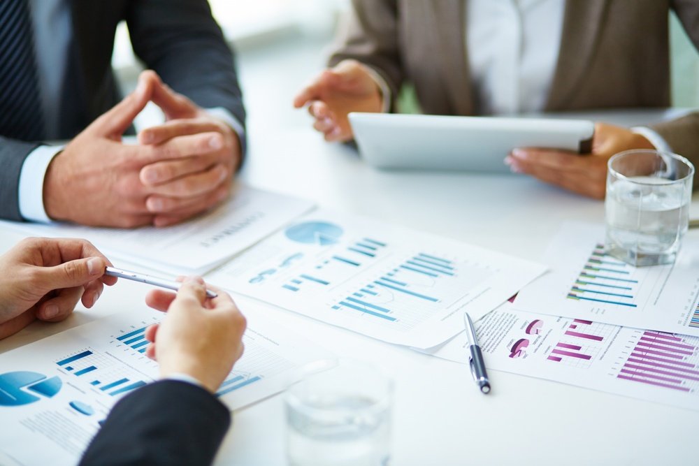 Équipe en réunion analysant des documents et graphiques pour le pilotage de l'entreprise.